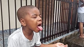 Mayotte, I bambini, con gli occhi chiusi, cercano di bere l'acqua piovana tirando fuori la lingua.