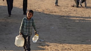 طفل فلسطيني يحمل أوعية مياه بلاستيكية على طريق ترابي في خان يونس، قطاع غزة، السبت، 21 ديسمبر، 2024.