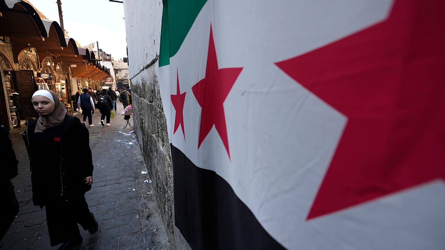 امرأة تمر بجوار العلم "الثورة" السورية المعلق على جدار في دمشق القديمة، سوريا، السبت 21 ديسمبر 2024.