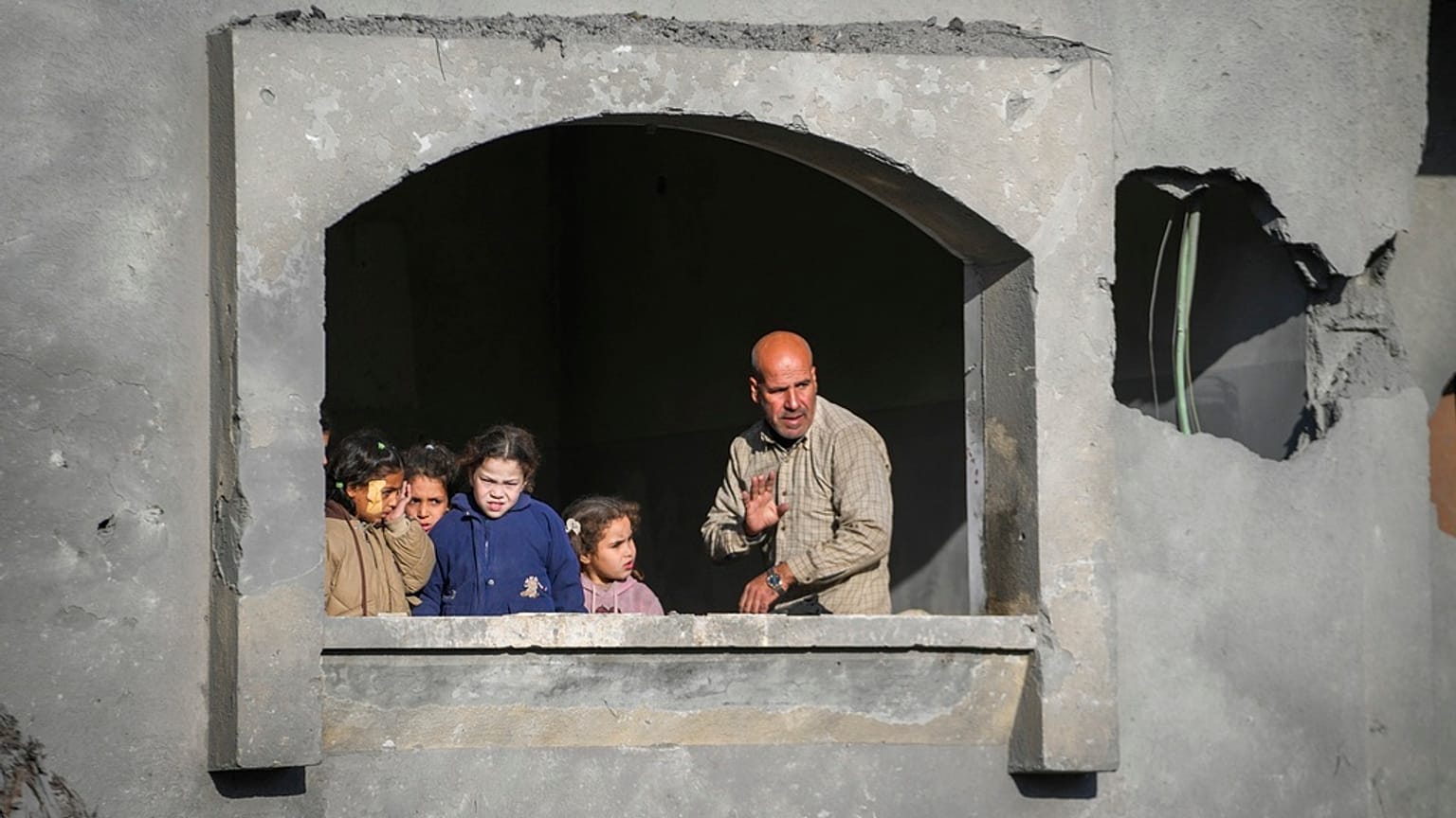 Gazze Şeridi'nin merkezinde, Deyr El Belah'ta İsrail saldırıları sırasında harabe hale gelmiş bir evin penceresinden dışarı bakan çocuklar ve bir adam, 22 Aralık 2024