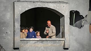 Gazze Şeridi'nin merkezinde, Deyr El Belah'ta İsrail saldırıları sırasında harabe hale gelmiş bir evin penceresinden dışarı bakan çocuklar ve bir adam, 22 Aralık 2024