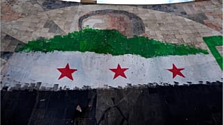 طفل سوري يقف تحت صورة عملاقة للرئيس السوري الراحل حافظ الأسد مطلية بألوان علم الثورة في دمشق، سوريا، الخميس 26 ديسمبر 2024.