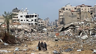 فلسطينيون يسيرون بجوار المبنى الذي دمره القصف الإسرائيلي لقطاع غزة في مدينة غزة يوم الأربعاء، 3 يناير، 2024.