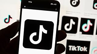 O logótipo do TikTok é apresentado num telemóvel em frente a um ecrã de computador que mostra uma página inicial do TikTok em Boston, 7 de maio de 2024