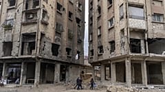 Des personnes marchent entre des bâtiments endommagés par des frappes aériennes pendant le règne d'Al-Assad à Douma, 29 décembre 2024.