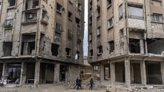 Des personnes marchent entre des bâtiments endommagés par des frappes aériennes pendant le règne d'Al-Assad à Douma, 29 décembre 2024.