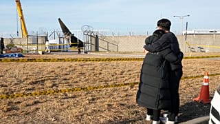 Imagen de dos ciudadanos surcoreanos junto al lugar en el que se estrelló un avión, en el Aeropuerto Internacional de Muan, Corea del Sur, el lunes 30 de diciembre de 2024.