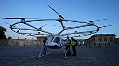 Pessoas juntam-se a um avião Volocopter antes de um voo de teste no último dia dos Jogos Olímpicos de verão de 2024, domingo, 11 de agosto de 2024, em Versalhes, França. 