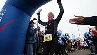 A belga ultrafutó Hilde Dosogne, középen, szurkolnak neki, amikor átlépi a célvonalat a 366. egymást követő maratonján a belgiumi Gentben, 2024. december 31-én, kedden.