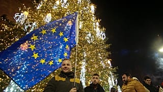 Ein Mann mit einer EU-Flagge steht neben einem Weihnachtsbaum in einer für die Weihnachts- und Neujahrsfeiern geschmückten Straße vor dem georgischen Parlament in Tiflis