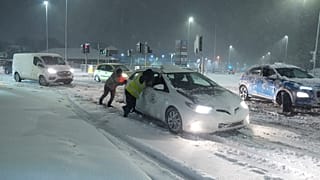 Persone aiutano a spingere le auto bloccate dalla neve a Leeds, in Inghilterra, domenica 5 gennaio 2025.