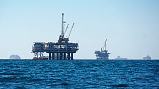 Фотография грузовых судов, стоящих на якоре в открытом море и делящих пространство с нефтяными платформами, перед заходом в порт Лос-Анджелеса в США