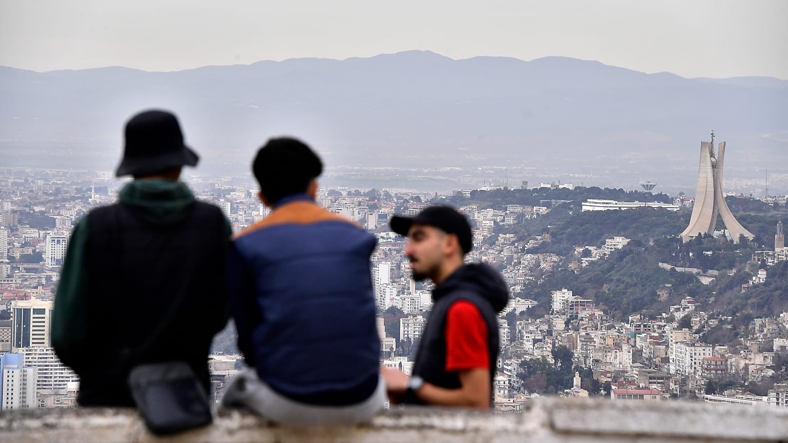 Bölge sakinleri konuşuyor, arka planda Şehitler Anıtı, sağda, 6 Ocak 2025 Pazartesi günü Cezayir'de. 