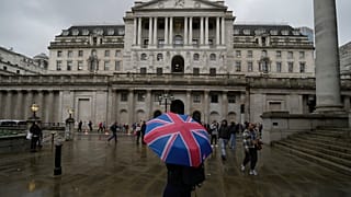 A woman with an umbrella stands in front of the Bank of England