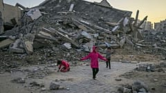 أطفال فلسطينيون يلعبون بجانب مبنى دمره الجيش الإسرائيلي في بلدة خان يونس وسط قطاع غزة، في 1 يناير 2025. 