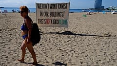 Una mujer camina frente a una señal que reza '¡No queremos turistas en nuestros edificios! Esto no es un resort de playa'