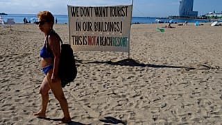 Una mujer camina frente a una señal que reza '¡No queremos turistas en nuestros edificios! Esto no es un resort de playa'