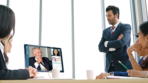 Video call in an office environment, with an older male executive seen smiling on the screen