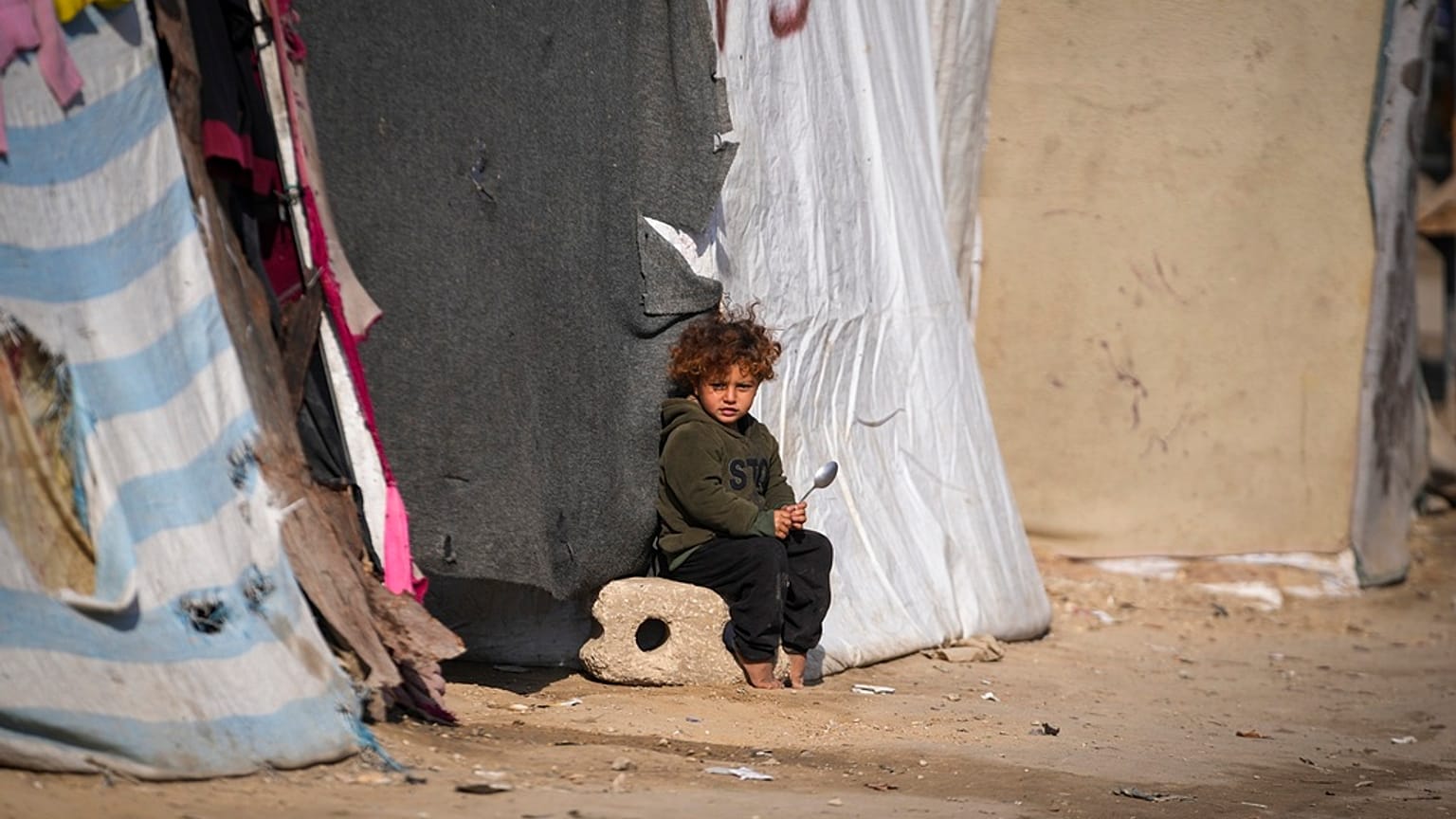طفل يجلس أمام خيمة بمخيم للنازحين الفلسطينيين في دير البلح، وسط قطاع غزة، الجمعة 17 يناير 2025.