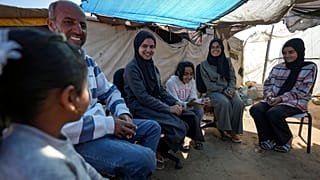 أفراد عائلة أبو جراد يجتمعون أمام خيمتهم بمنطقة المواصي، جنوب قطاع غزة، يوم السبت، 18 يناير 2025.