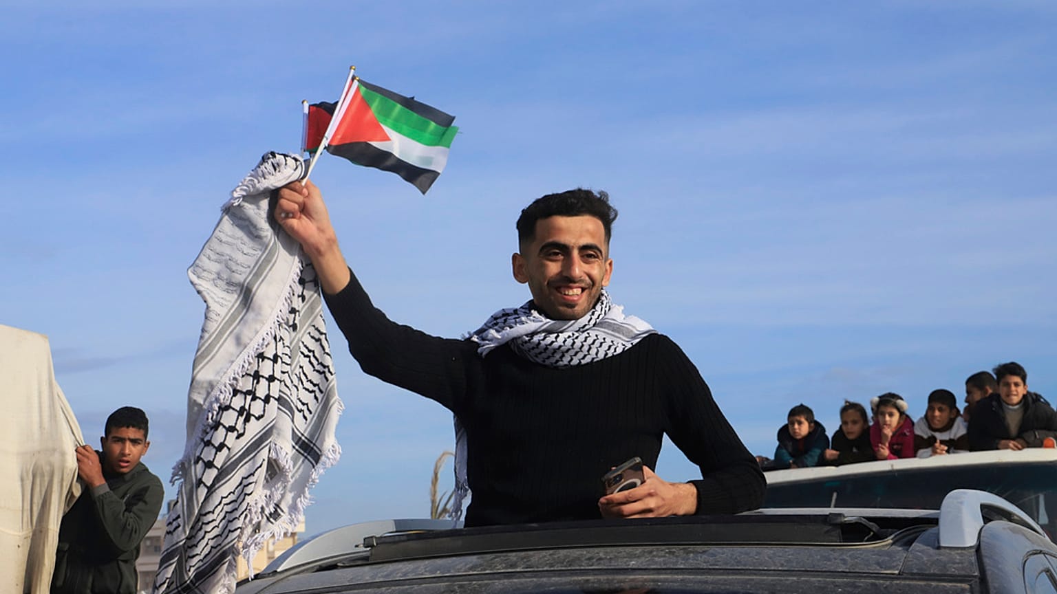 فلسطينيون نازحون يلوحون بالعلم الفلسطيني أثناء عودتهم إلى رفح، بينما دخل اتفاق وقف إطلاق النار في رفح، قطاع غزة، الأحد، 19 يناير/كانون الثاني2025