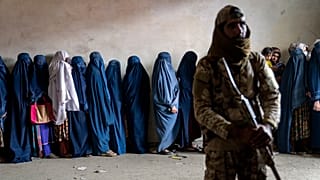 Ein Taliban-Kämpfer steht Wache, während Frauen darauf warten, Lebensmittelrationen zu erhalten, die von einer humanitären Hilfsorganisation in Kabul verteilt werden, 23. Mai 2023