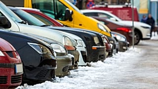 Una fila di auto parcheggiate su una strada innevata. 