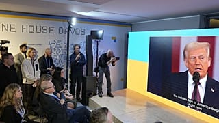 Menschen verfolgen die Amtseinführungsrede von Donald Trump auf Bildschirmen im Haus der Ukraine am Rande des Weltwirtschaftsforums in Davos, Schweiz, Montag, 20. Januar 2025