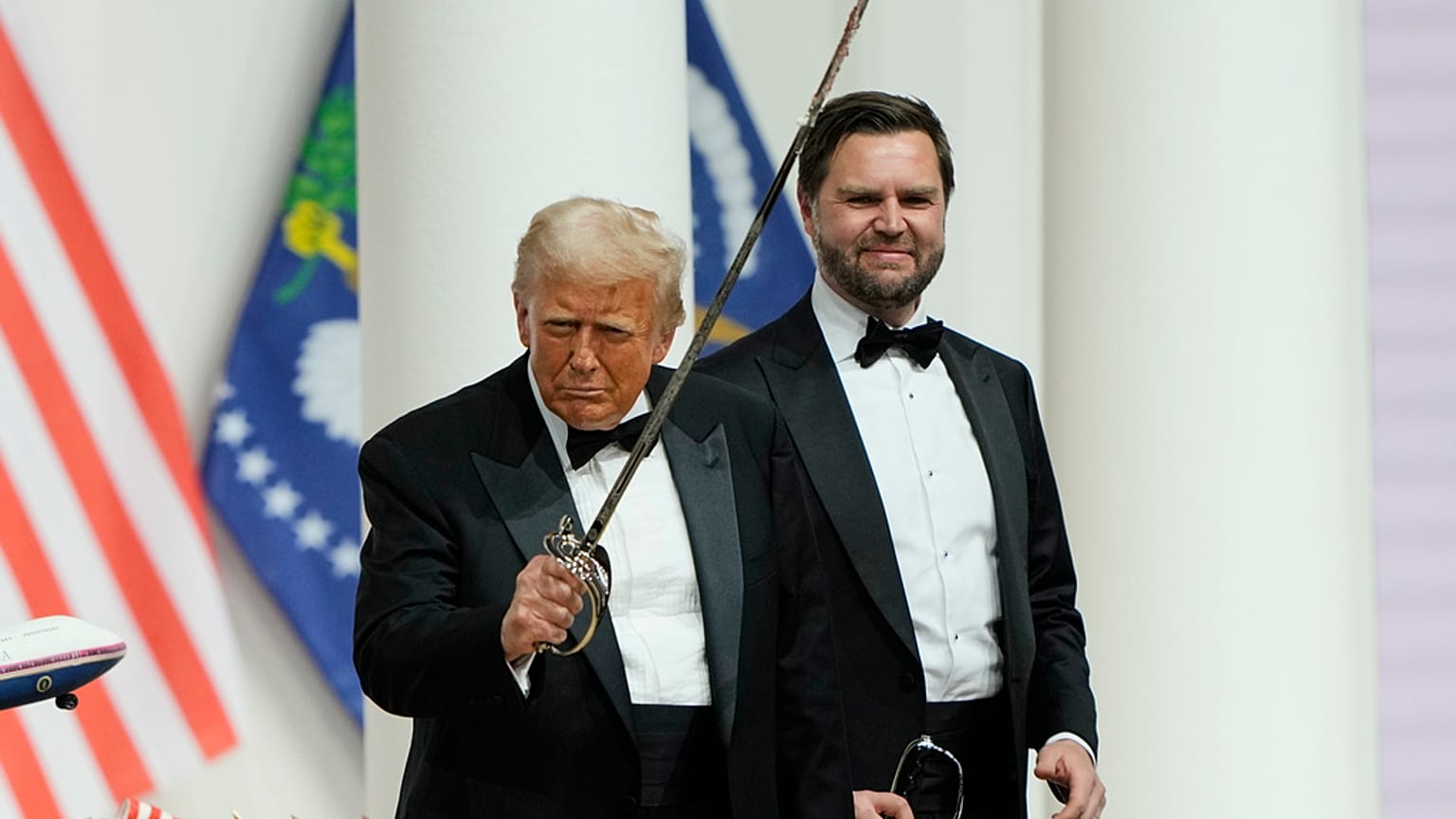El presidente Donald Trump, a la izquierda, sostiene un sable después de usarlo para cortar una tarta en el Baile del Comandante, parte de la 60ª Inauguración Presidencial.