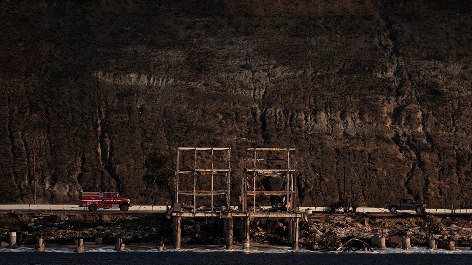 A firetruck and a pickup truck move past homes destroyed by the Palisades Fire along the coastline, Friday, Jan. 17, 2025, in Malibu, Calif.