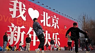 Cinesi giocano a fare gli otturatori vicino a un enorme tabellone con la scritta "I Love Beijing, Happy New Year 2025", a Pechino