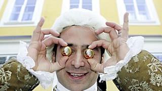 Mozart kılığına girmiş Benjamin Dzialowski, 27 Ocak 2006 Cuma günü Salzburg kentinde Mozart'ın doğduğu evin önünde Mozart toplarını gözlerine karşı tutuyor