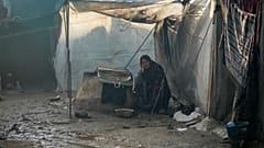 سميرة ضيف الله، 52 عامًا، نازحة من مدينة غزة، تجلس خارج خيمتها بعد ليلة من هطول الأمطار الغزيرة في دير البلح وسط قطاع غزة، الخميس 23 يناير/كانون الثاني 2025