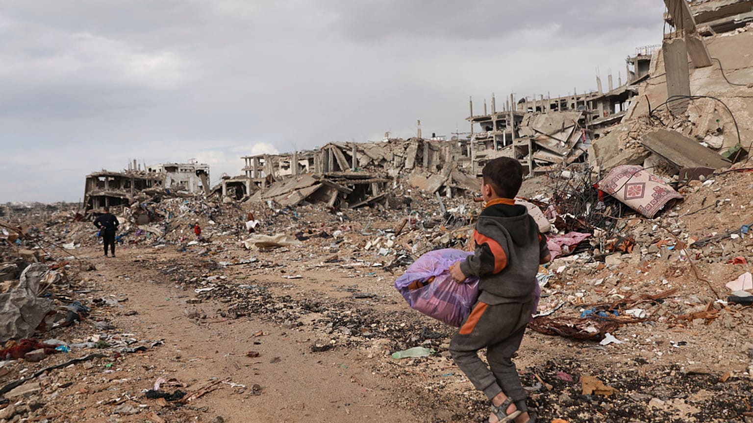 صبي فلسطيني يحمل أغراضه بجانب أنقاض المنازل المدمرة، في مدينة غزة، قطاع غزة، الجمعة، 24 يناير/كانون الثاني 2025.
