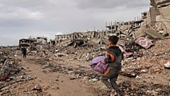صبي فلسطيني يحمل أغراضه بجانب أنقاض المنازل المدمرة، في مدينة غزة، قطاع غزة، الجمعة، 24 يناير/كانون الثاني 2025.