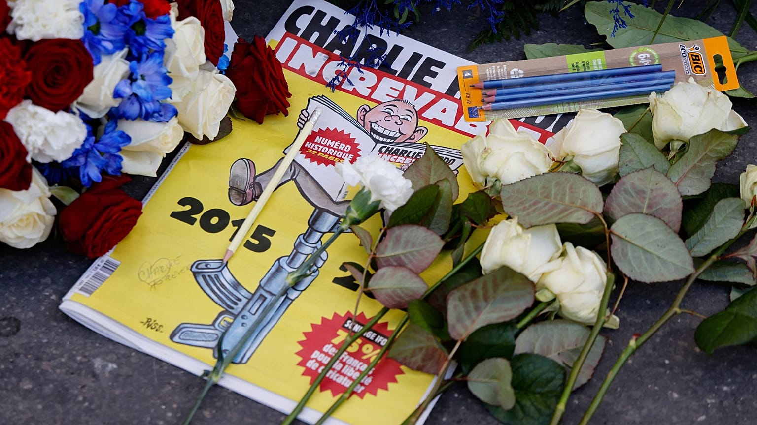 A Charlie Hebdo francia szatirikus újság különkiadása a Charlie Hebdo egykori irodája előtt elhelyezett koszorúk és ceruzák között, 2025. január 7-én.