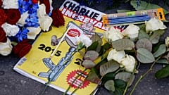 Fransız hiciv gazetesi Charlie Hebdo'nun özel bir baskısı, Charlie Hebdo'nun eski ofislerinin önüne bırakılan çelenk ve kalemlerin arasında duruyor, 7 Ocak 2025.