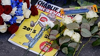 Fransız hiciv gazetesi Charlie Hebdo'nun özel bir baskısı, Charlie Hebdo'nun eski ofislerinin önüne bırakılan çelenk ve kalemlerin arasında duruyor, 7 Ocak 2025.