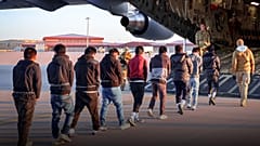Bellerinden zincirlenmiş kişilerin bir askeri uçağa bindirildiği görülüyor