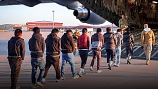 Bellerinden zincirlenmiş kişilerin bir askeri uçağa bindirildiği görülüyor