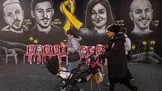 İnsanlar 24 Ocak 2025 Cuma günü Kudüs'te, Gazze Şeridi'nde Hamas tarafından tutulan rehinelerin portrelerinden oluşan bir duvar resmi ve enstalasyonun önünden yürüyerek ve koşarak geçiyor. 