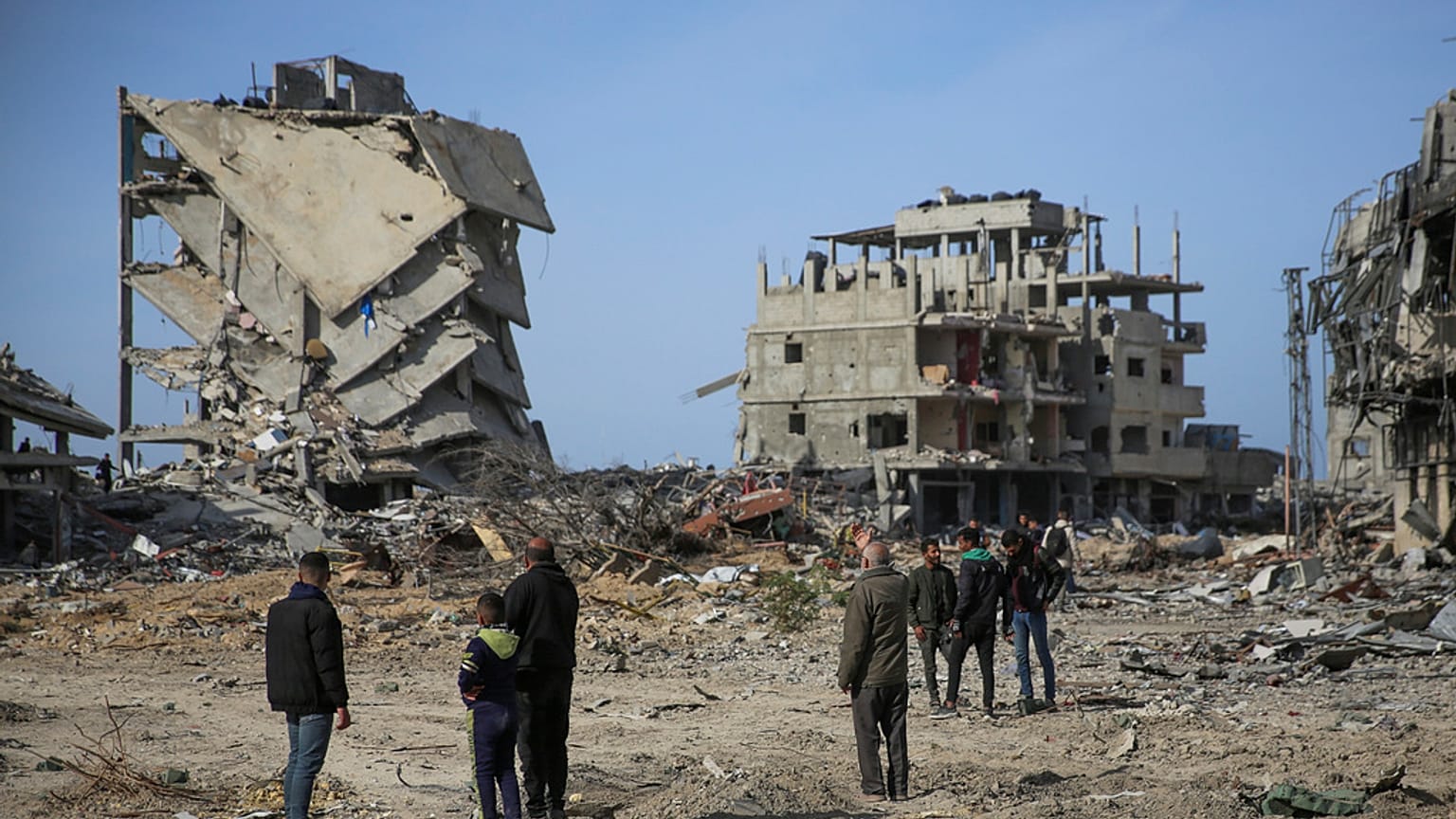 فلسطينيون يقفون بالقرب من المباني التي دمرها الهجوم الجوي والبري الإسرائيلي، 19 يناير، 2025، في رفح. 