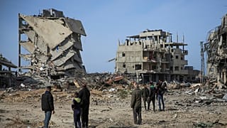 فلسطينيون يقفون بالقرب من المباني التي دمرها الهجوم الجوي والبري الإسرائيلي، 19 يناير، 2025، في رفح.
