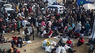 Palestinianos deslocados reúnem-se com os seus pertences perto de um bloqueio de estrada enquanto esperam para regressar às suas casas na parte norte da Faixa de Gaza, 26 de janeiro de 2025