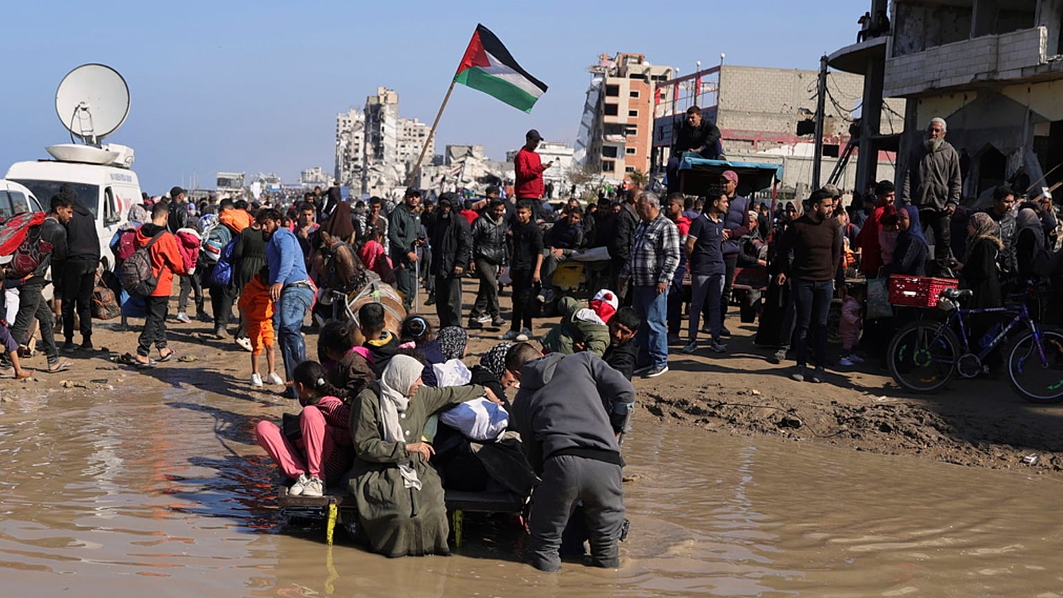 أسرة فلسطينية تحاول عبور بركة مياه أثناء عودة النازحين إلى منازلهم في شمال قطاع غزة، الاثنين، 27 يناير 2025. 