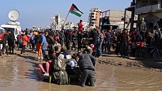 أسرة فلسطينية تحاول عبور بركة مياه أثناء عودة النازحين إلى منازلهم في شمال قطاع غزة، الاثنين، 27 يناير 2025. 