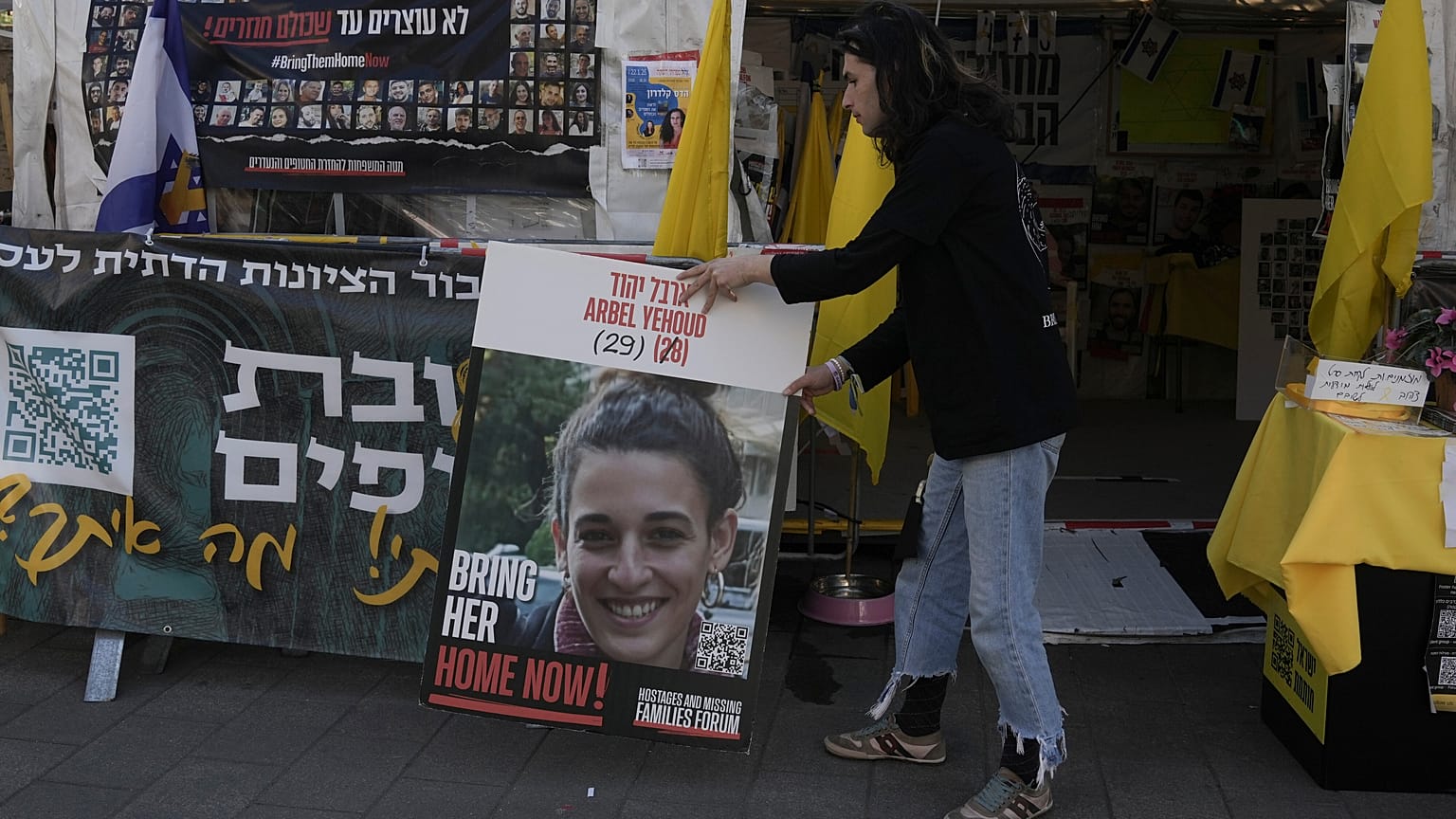 Ein Mann legt ein Foto von Arbel Yehoud neben ein hebräisches Transparent, auf dem die Rückkehr der von der Hamas im Gazastreifen festgehaltenen Geiseln gefordert wird, Montag, 27. Januar 2025.