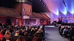Menschen nehmen an der Erinnerungsveranstaltung zur Befreiung von Auschwitz teil