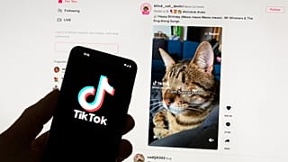 The TikTok logo is seen on a mobile phone in front of a computer screen which displays the TikTok home screen, on March 18, 2023.