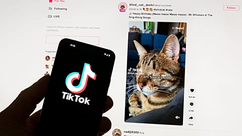 The TikTok logo is seen on a mobile phone in front of a computer screen which displays the TikTok home screen, on March 18, 2023.